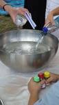 Taufschüssel aus Edelstahl. Mehrere Hände schütten aus kleinen Flaschen Wasser in die Schüssel.