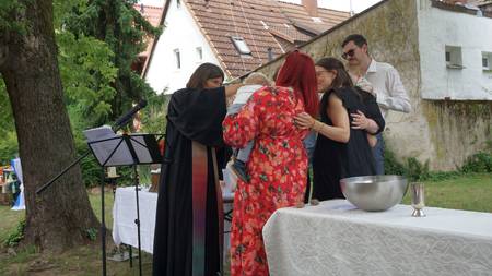 Pfarrerin Bindseil tauft zwei Babys am Altar im Kirchgarten. Die Familie  umringt die Täuflinge.