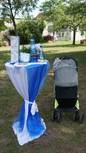 Stehtisch mit Taufkerze und Geschenken im Garten, daneben Kinderwagen